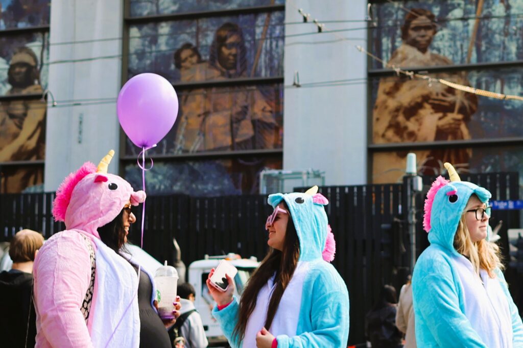 Women in colorful unicorn costumes standing in front of a Melbourne mural depicting Aboriginal people.